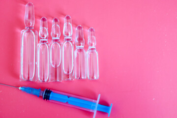 Glass ampoules and a syringe are placed on a bright pink background, symbolizing medical procedures...