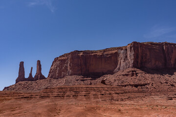 Fototapeta premium The Three Sisters spires in Monument Valley on the Colorado Plateau, Arizona. De Chelly Sandstone with Organ Rock Formation / Shale. A mesa is a flat-topped mountain or hill. Mitchell Mesa. Pinnacle