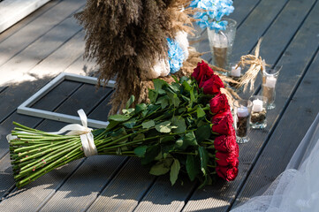 Large bouquet of red roses rests on a wooden deck, near decorative elements.