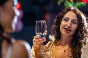 Two female friends enjoy a deep conversation over a glass of wine at a party or bar A concept for...