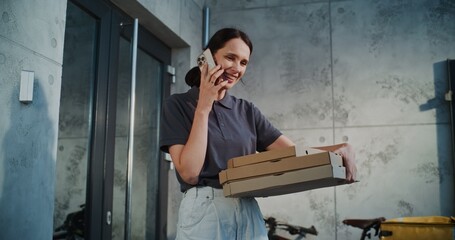 Delivery Woman Standing near Office Building with Pizza in Cardboard Boxes, Notifying Client by Phone about Successful Delivery. Woman Working in Pizza Delivery Service, Delivering Restaurant Food.