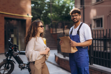 Delivery man delivering a package to a woman with electric scooter on the street