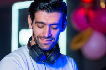 A handsome DJ focuses on his music set in a vibrant nightclub with a guest in the background A...