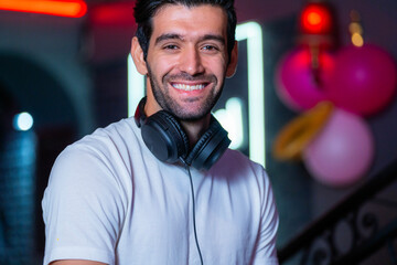 A handsome DJ focuses on his music set in a vibrant nightclub with a guest in the background A...