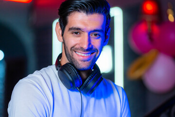 A handsome DJ focuses on his music set in a vibrant nightclub with a guest in the background A...