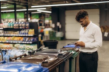 Man Using Phone Near Recycling Bins in a Bright Market