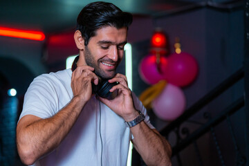 A handsome DJ focuses on his music set in a vibrant nightclub with a guest in the background A...