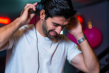 A handsome DJ focuses on his music set in a vibrant nightclub with a guest in the background A...