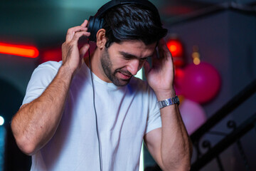 A handsome DJ focuses on his music set in a vibrant nightclub with a guest in the background A...