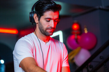 A handsome DJ focuses on his music set in a vibrant nightclub with a guest in the background A...
