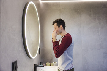 Young man flosses his teeth in front of a bathroom mirror, focusing on oral hygiene as part of a...