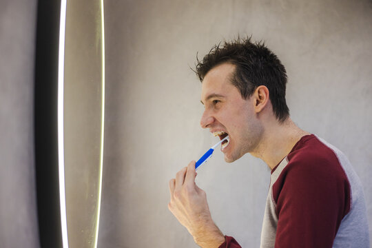 Young man focused on dental hygiene, brushing his teeth in front of a mirror as part of a healthy daily routine in a clean, modern bathroom setting. - Powered by Adobe