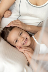 Mother and daughters cuddling, smiling, dancing and having fun in bedroom. Little girl resting in mom's arms. Vintage bed with curtains in bright interior.