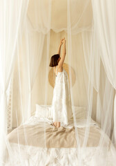 Delicate woman in long white dress sitting on floor with head on bed. Female dancing and relaxing...