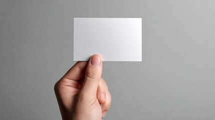 This image depicts a hand holding a blank white card against a neutral background, offering a simple yet versatile concept perfect for various creative uses. High quality