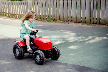 Little girl riding a toy tractor on a farm in the country