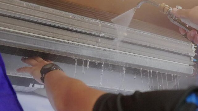 Air- con technician using high pressure water gun for cleaning air conditioner