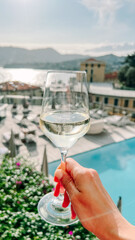 Hand holding wine glass by pool with sea view in Rapallo