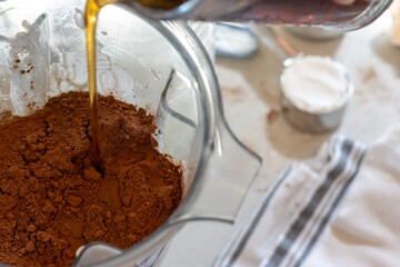Maple syrup poured over cocoa, eggs and batter in blender jar