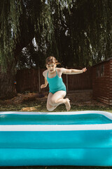 Child girl jumping into inflatable pool in backyard.