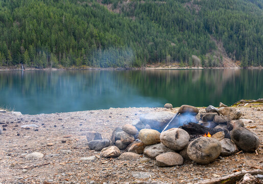 Campfire by the lake surrounded by forest on a calm day