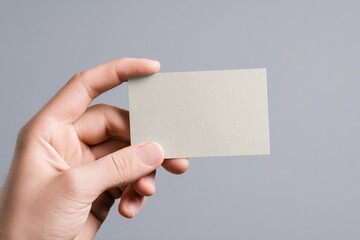 A hand holds a blank, light beige business card against a neutral gray background. High quality