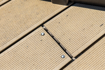 Damaged composite decking boards with visible cracks due to poor installation. Close-up of light brown planks with metal screws and misaligned joints.