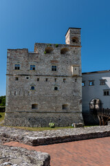 Stone tower of Sárospatak Castle in Hungary with small windows, medieval walls, and wooden bridge, under clear blue sky.
