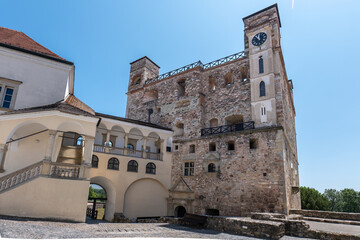 Sarospatak castle courtyard with historic stone tower and clock, arched gallery, and cobblestone path under clear blue sky in Hungary.