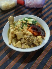 A Bowl of Delicious Chicken Noodles with Complete Toppings: Chicken Pieces, Dumplings, Meatballs, Green Mustard Greens, and Sprinkled with Spring Onions