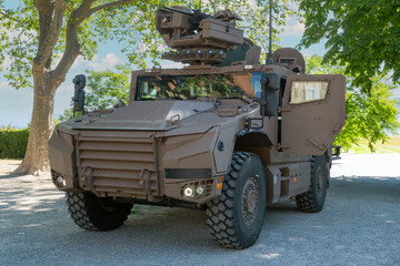 French military vehicle with a gun on top. The vehicle is brown. It is parked in a parking lot