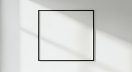 A minimalist black frame hangs on a white wall, illuminated by soft sunlight.