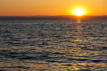 The sun is setting over the ocean, casting a warm glow on the water