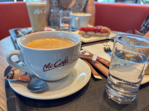 Parndorf, Austria - 25 May 2025: close-up of a mccafe coffee cup with a glass of water and dessert, concept of cafe, relaxation, bakery