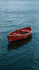 Minimalist Aerial View of Red Wooden Rowboat Floating in Calm Deep Blue Water with Gentle Ripples