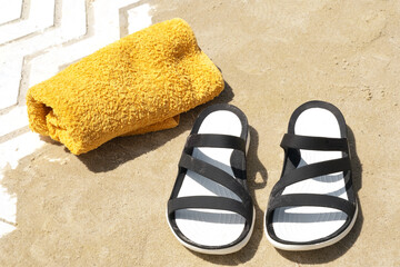 Black sandals and a yellow towel resting on sandy beach during a sunny day