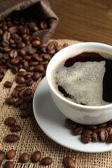 Aromatic coffee in cup and beans on table, closeup