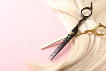 Hair strand and scissors on light pink background, closeup. Space for text