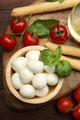 Tasty mozzarella cheese balls, breadsticks, tomatoes and basil on wooden table, flat lay