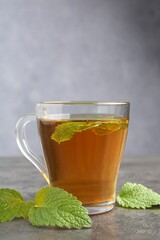 Aromatic lemon balm tea in glass cup and fresh leaves on gray textured table
