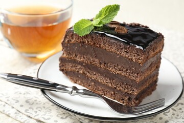 Piece of chocolate cake served with mint, fork and tea on table, closeup