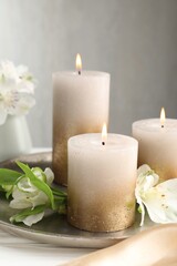 Burning candles and beautiful flowers on white table, closeup