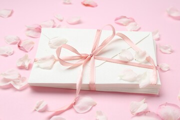 Stack of love letters and petals on pink background, closeup