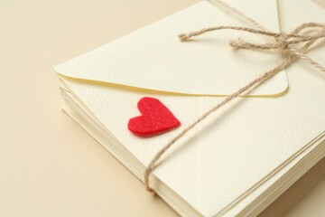 Stack of love letters and red heart on beige background, closeup