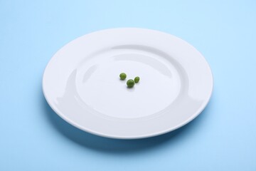 Plate with fresh green peas on light blue background, closeup