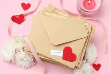 Stack of letters with phrase I Love You, flowers, burning candle and red hearts on pink background,...