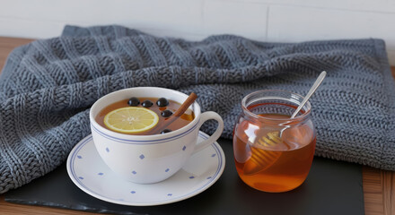 A cup of hot tea with lemon, cinnamon, and honey against a cozy knitted blanket background.