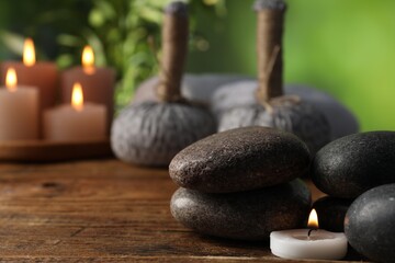 Spa composition with stones and burning candle on wooden table against blurred green background,...