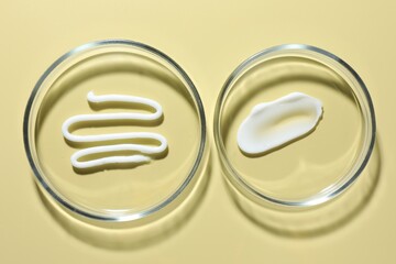 Different cosmetic products in Petri dishes on pale yellow background, flat lay