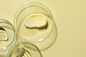 Different cosmetic products in Petri dishes on pale yellow background, flat lay. Space for text